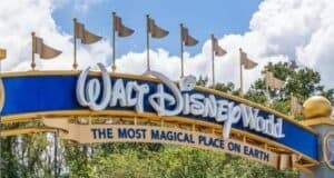 Entrance sign to Walt Disney World with a blue and gold design, featuring the phrase "The Most Magical Place on Earth." The sky is partly cloudy, and trees are visible in the background.