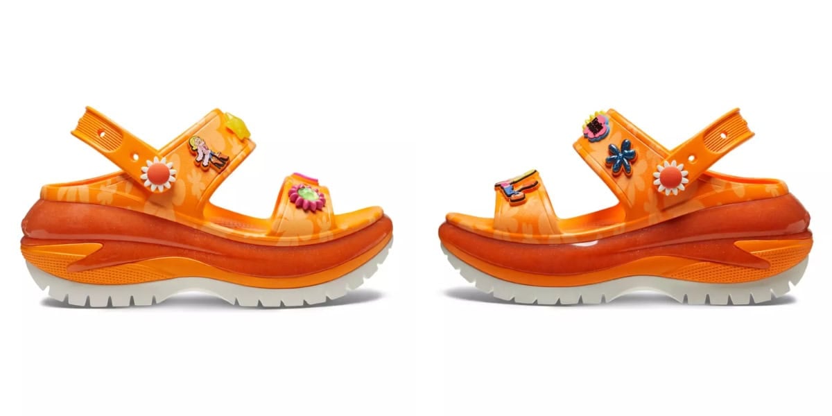 A pair of bright orange sandals with thick soles and decorative floral and insect designs. The straps are embellished with colorful charms, and the soles are white with a textured pattern. The sandals have an open-toe design.