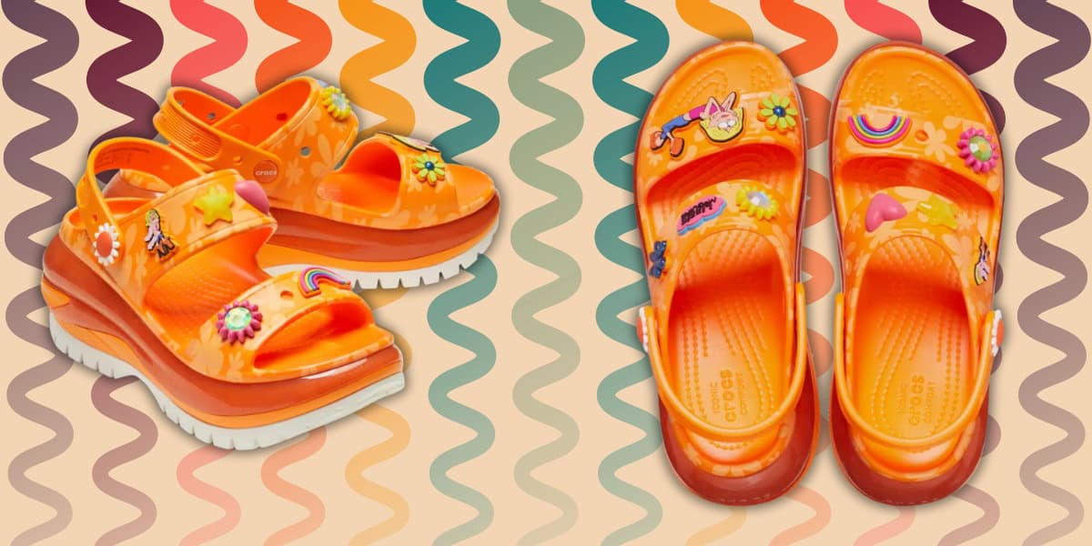 Orange platform sandals with playful decorations, including rainbows, flowers, and characters, placed against a wavy orange and purple patterned background. The sandals have white soles and a sporty design.