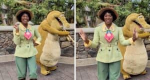A person wearing a green outfit and hat, dances joyfully alongside someone in an alligator costume. They are outdoors, with a stone wall and greenery in the background, exuding a lively and cheerful atmosphere.