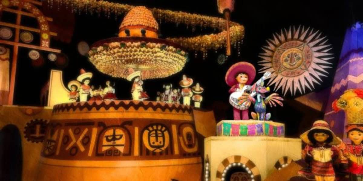 A vibrant scene with animatronic figures in colorful traditional Mexican attire playing instruments. The background features cultural symbols and decorations, including a large sombrero and sun motif, all illuminated with bright, festive lighting—perfectly capturing the spirit of Disneyland 70th celebrations.