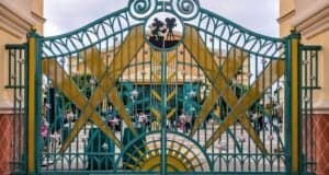 Ornate green and gold gate with star decorations at an amusement park entrance. People are visible in the background near the check-in area. The sky is overcast, creating a soft, diffused light.