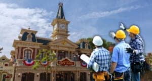 Three construction workers wearing helmets and holding blueprints discuss the architecture of a building resembling a decorative town hall with a clock tower under a clear blue sky. The building has red brick, white columns, and American flag bunting inside of Magic Kingdom, near the Rivers of America location at Walt Disney World Resort.