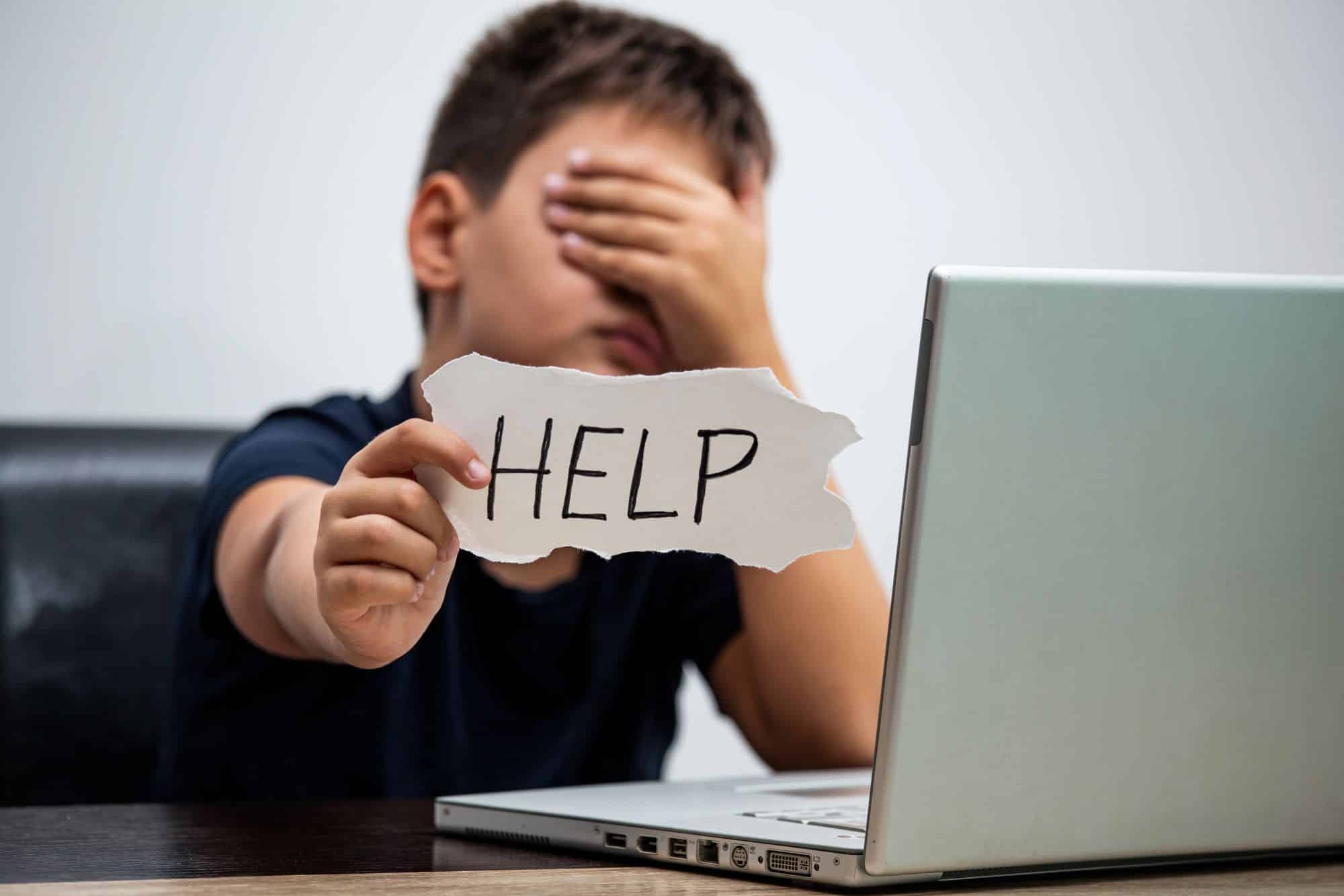 a boy holding a piece of paper with text help over his face