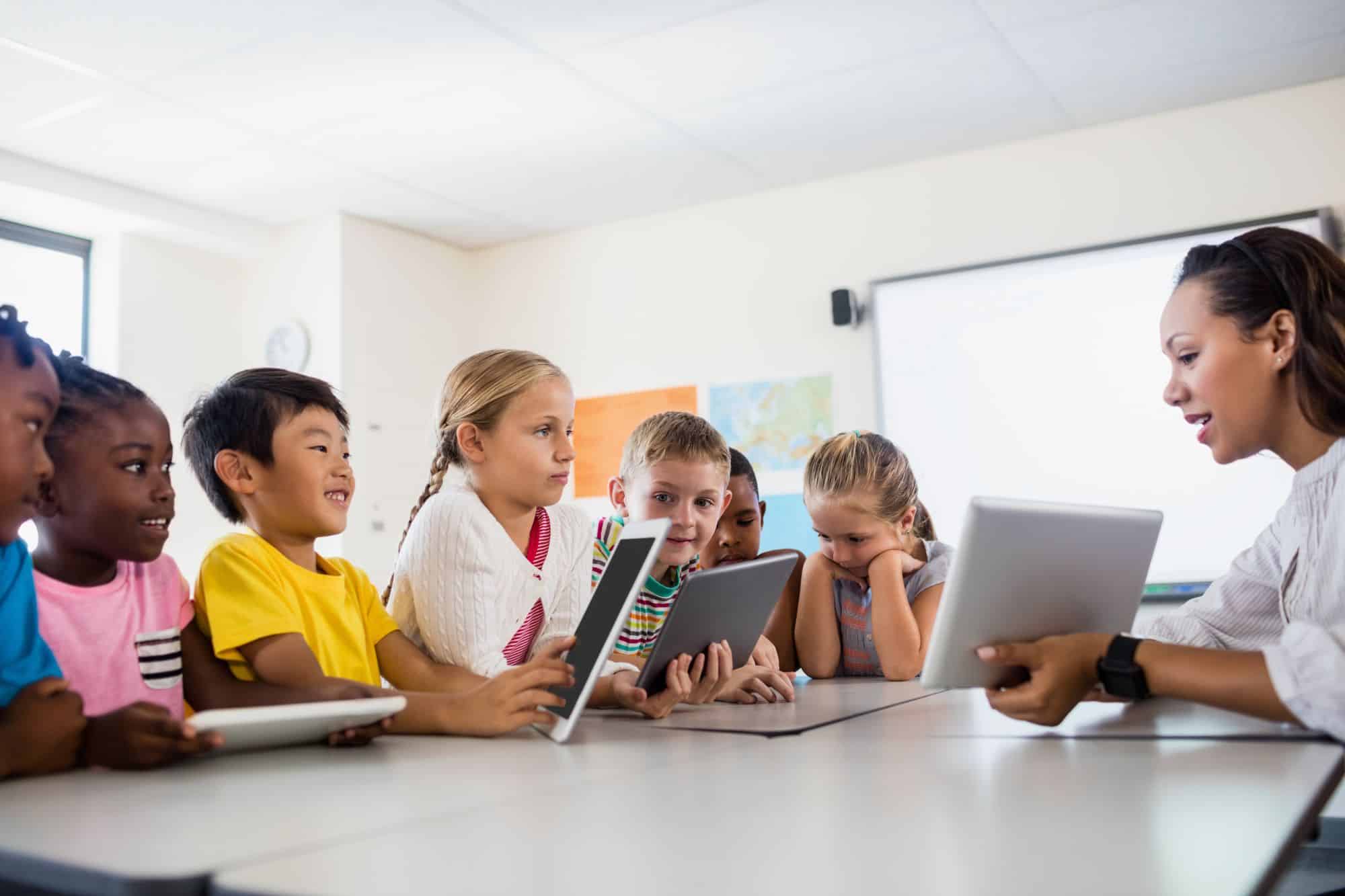 a group of children sitting at a table with a tablet PCs