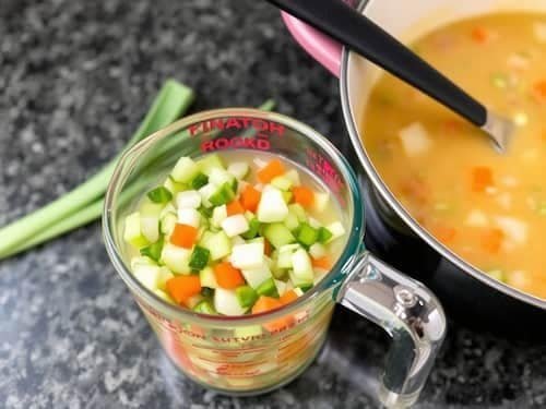 A measuring cup filled with chopped vegetables next to a pot of soup, ideal for preparing the cabbage soup diet recipe or the 7-day cabbage soup diet.