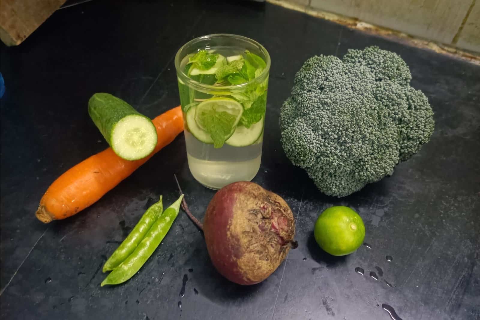 Fresh vegetables including carrot, cucumber, beetroot, broccoli, green peas, lime, and a glass of mint-infused water for a healthy detox diet.