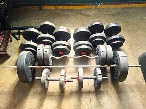 Gym equipment including dumbbells, barbells, and weight plates for a home workout, ideal for a beginner's gym schedule.