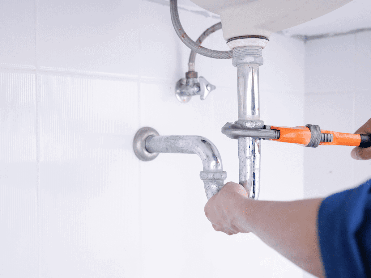 close up of a plumber tightening a pipe under a sink