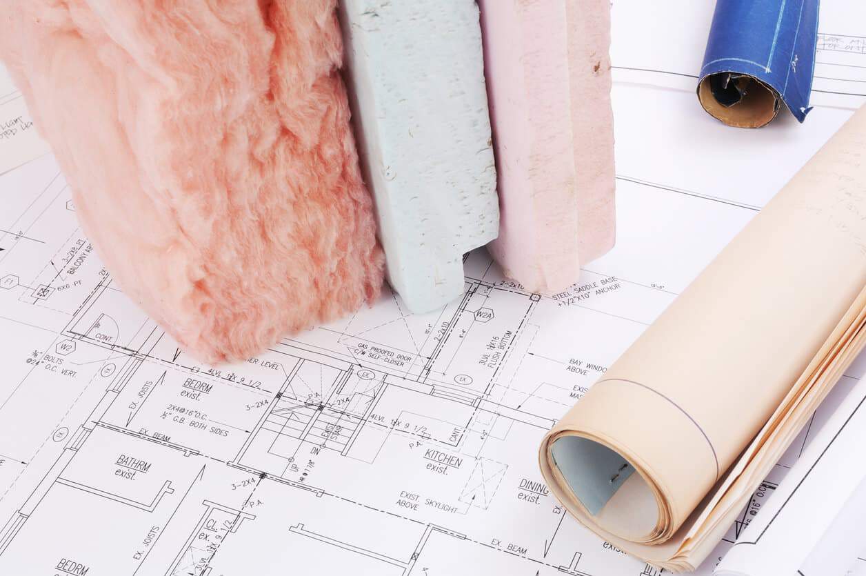Various building insulation materials and rolled blueprints neatly arranged on top of architectural plans, illustrating a meticulous approach to home insulation that effectively complements the HVAC system.