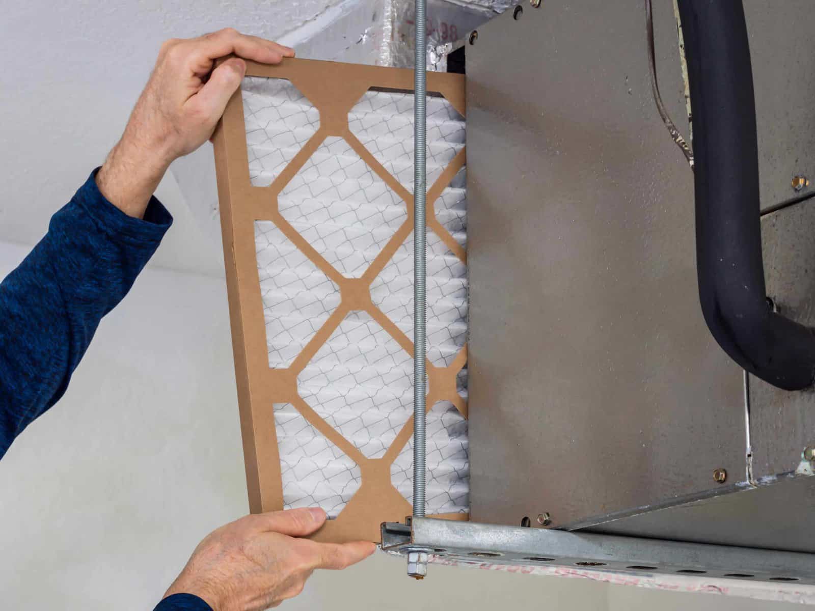 A person replaces an air filter in the HVAC system, carefully inserting it into the metal compartment, mindful of any critters that might have made a home inside.