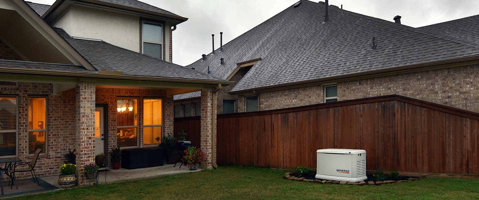A permanent backup generator sits in a backyard, nestled beside a brick house with wooden fencing, ready to provide reliable power on this cloudy day.