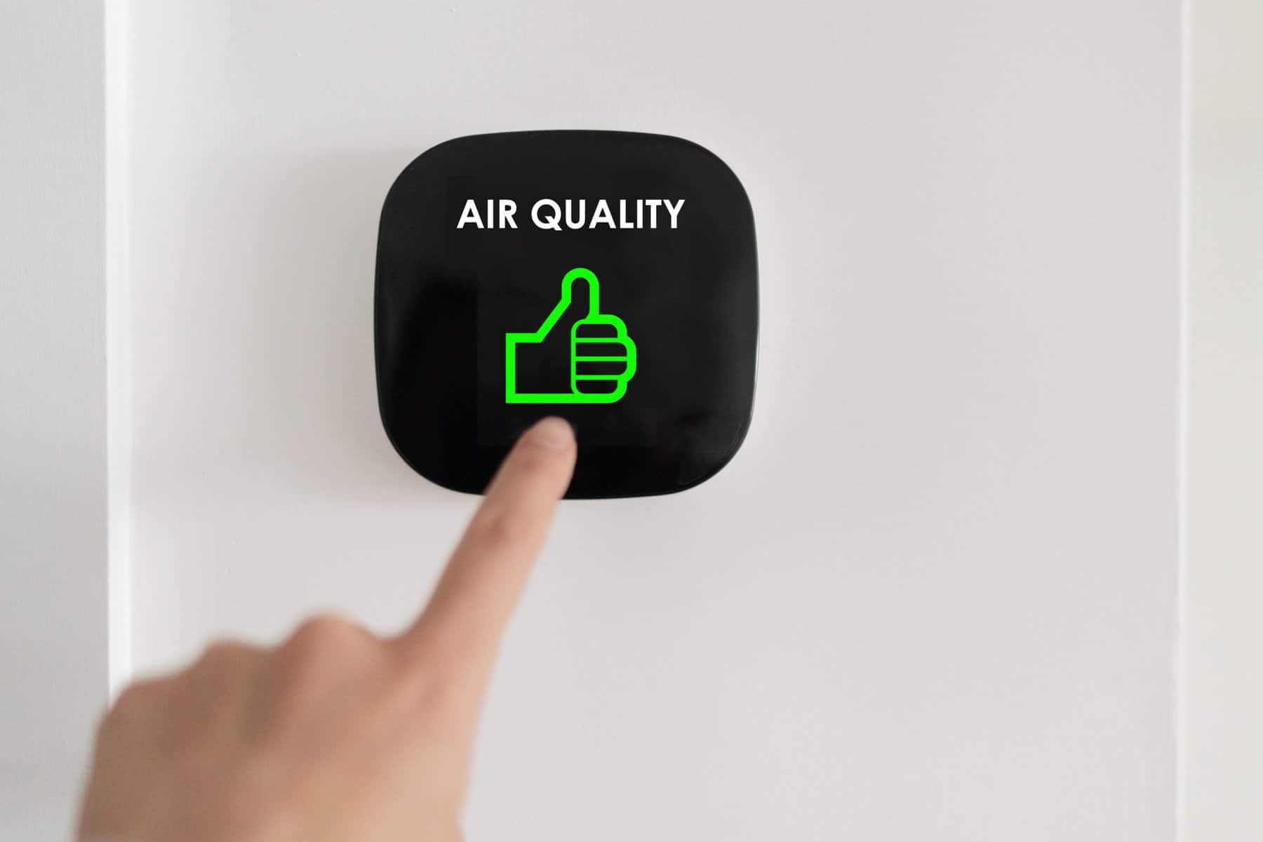 A hand points to a black air quality device on a white wall, displaying a green thumbs-up and the words "AIR QUALITY," offering tips for better air.