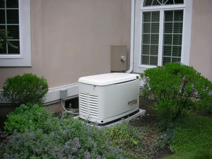 A standby generator, well-maintained and tucked beside green bushes near a window, ensures your home is always powered.