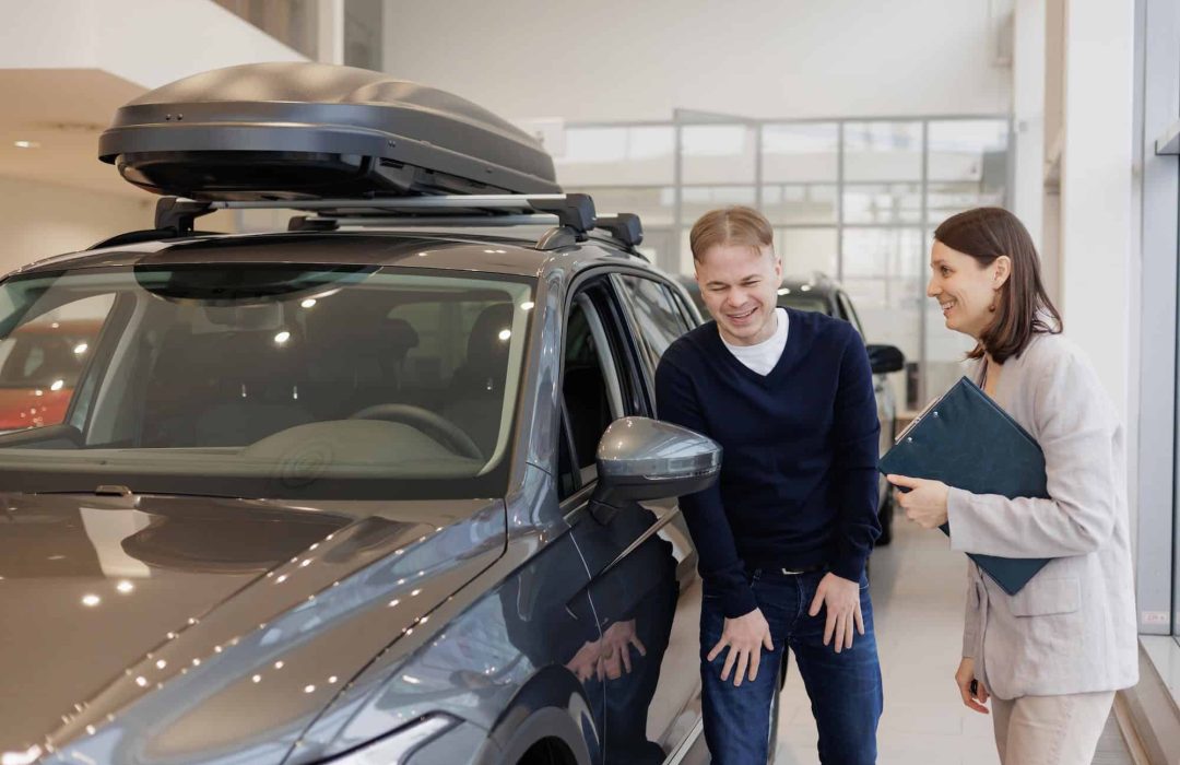 man buys a car at a car dealership. A female salesperson and car rental helps with the purchase