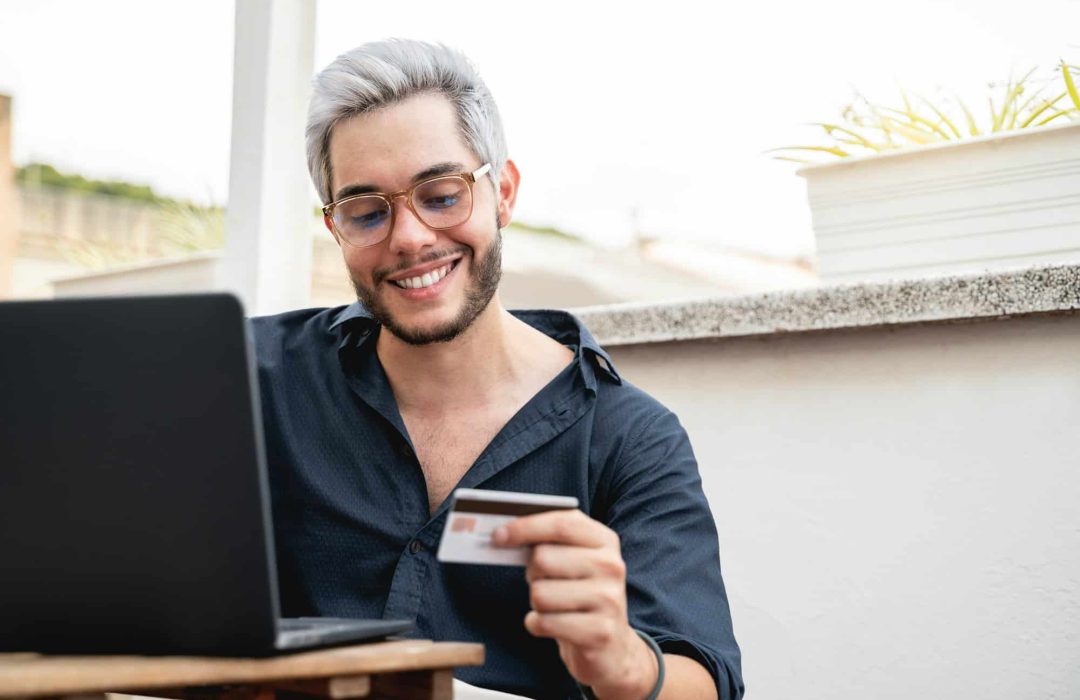 Young hipster man holding credit cart using computer laptop for online payment - E-commerce, bank