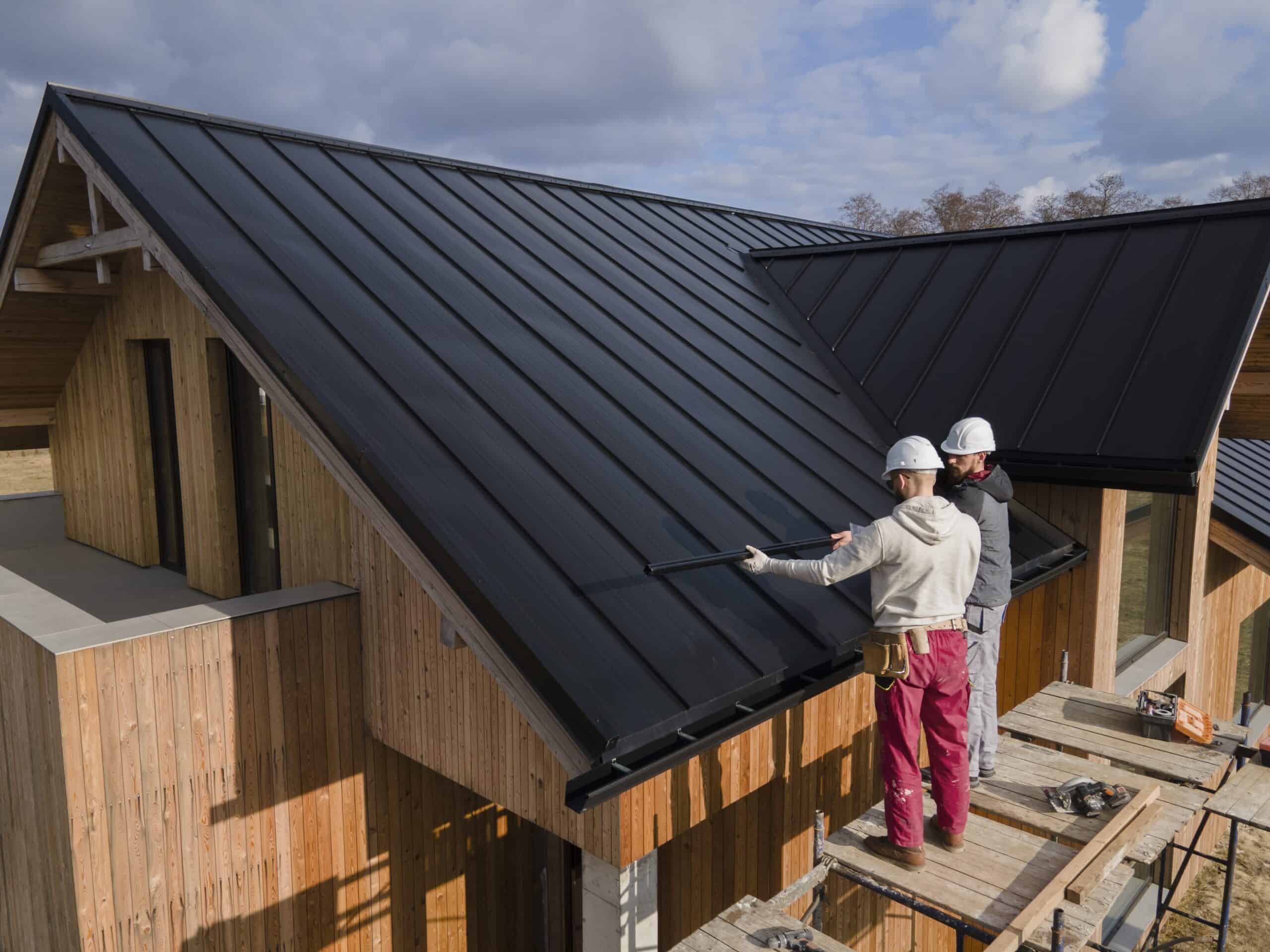 Hillside Metal workers apply protective coating to a metal roof on a house, showing roofing safety and care.