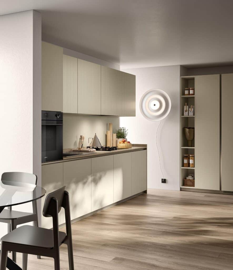 Modern kitchen with beige cabinets, built-in oven, gas stovetop, wall-mounted circular light fixture, and a small dining area with a glass table and chairs.