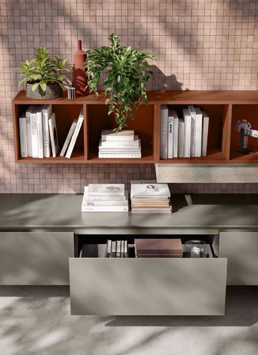 Stylish shelving with books, plants, and decorative items against a tiled wall; an open drawer reveals more books and a candle.