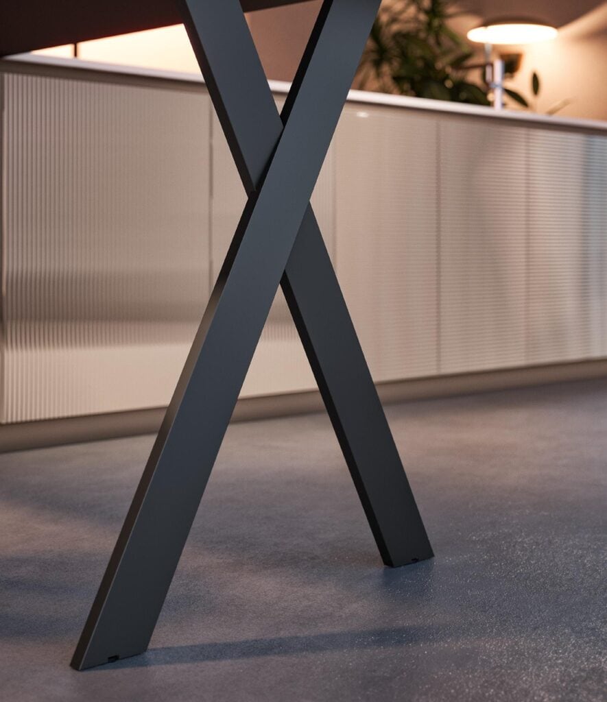 Close-up of a modern table leg with an X-shaped design against a background of a cabinet and table lamp.