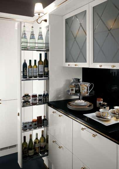 Modern kitchen with glass cabinet doors, a pull-out pantry revealing wine and condiment storage, and a black countertop with decorative dishes and cups.