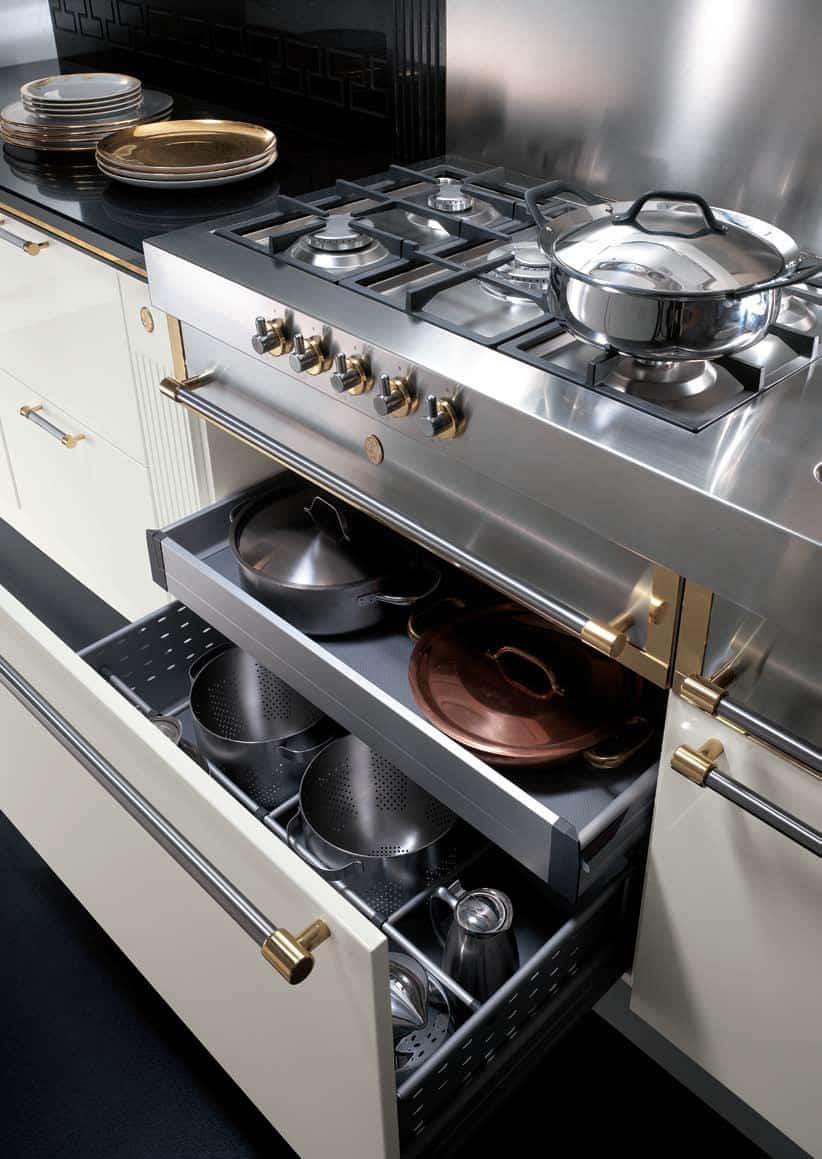 Modern kitchen with a stainless steel gas stove, open drawer containing metal pots and pans, and stacked plates on a countertop.