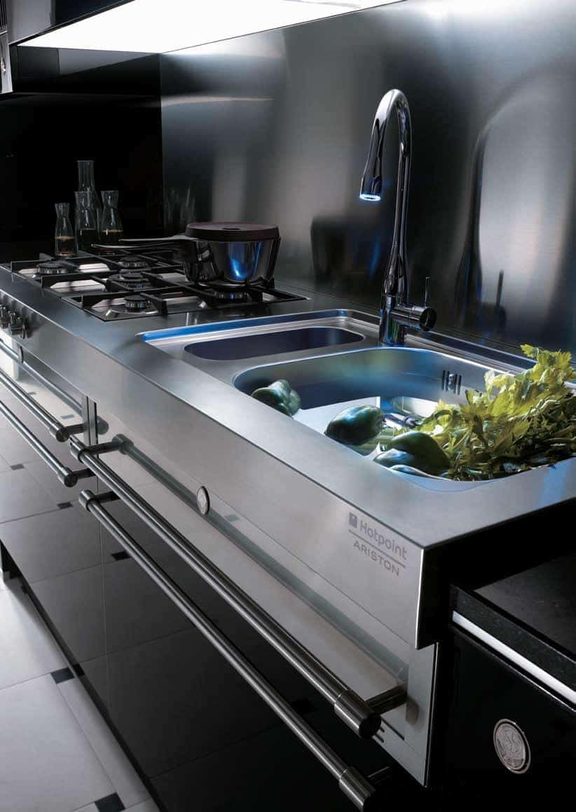 Modern stainless steel kitchen with a gas stove, sink, and faucet; vegetables are in the sink for washing.