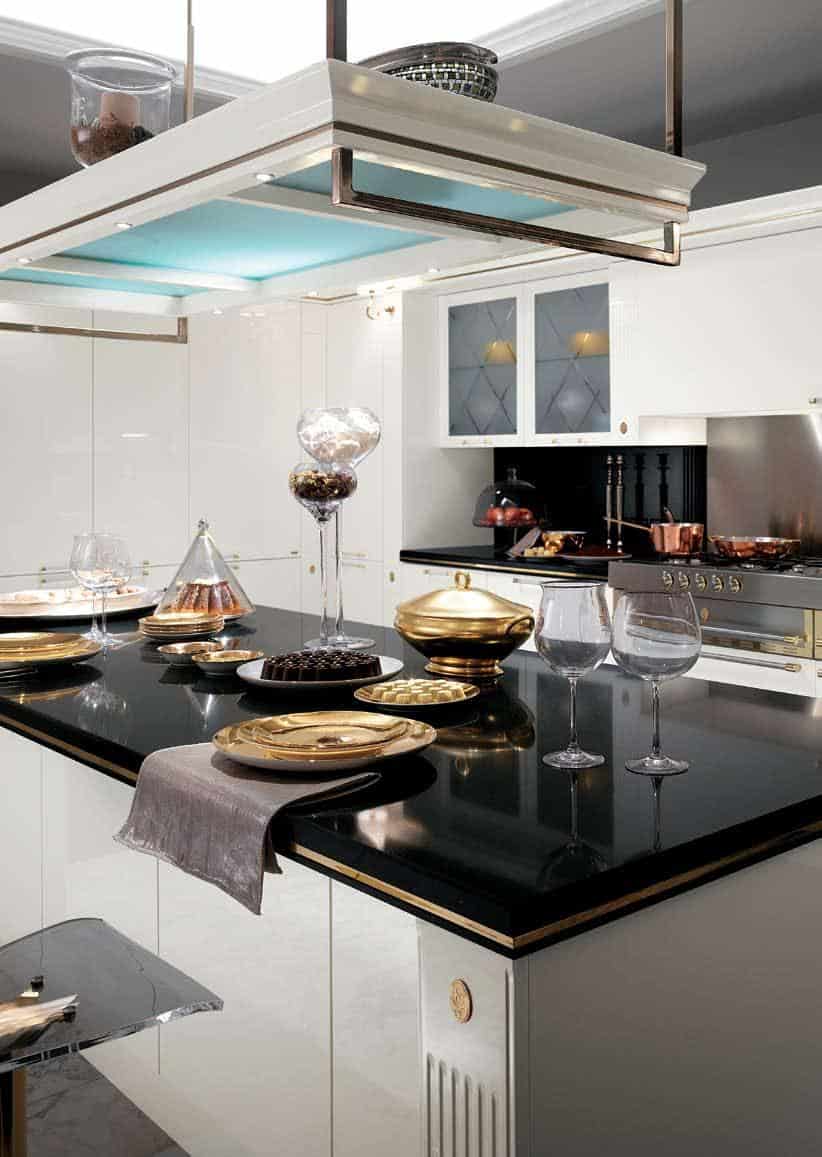 Modern kitchen with glossy black countertops, gold and black dishware, and centerpiece decorations, featuring sleek white cabinetry and a stainless steel stove.