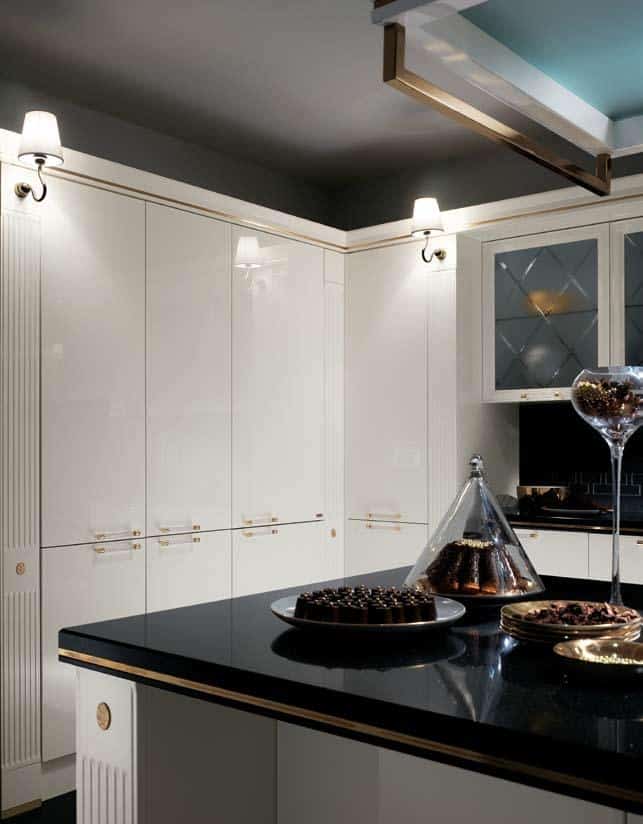 Elegant kitchen interior with white cabinets, a black countertop, and decorative lighting, featuring a plate of chocolates and a cake under a glass dome.