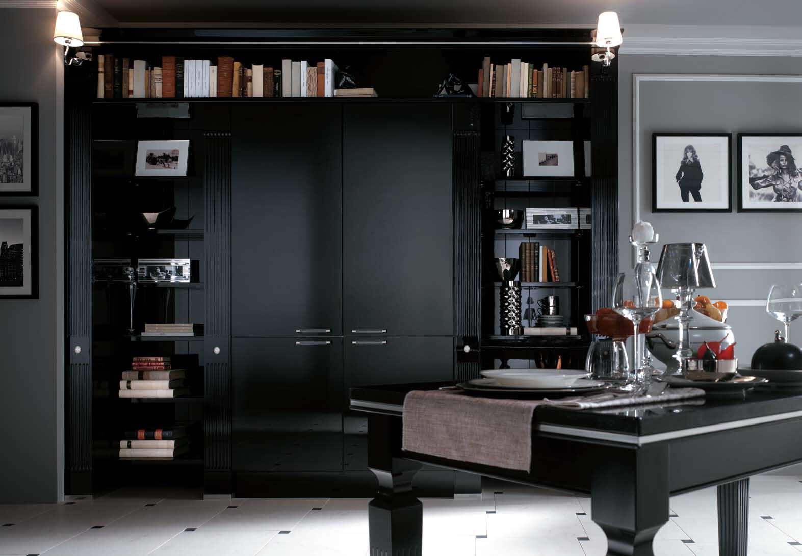 A stylish, modern kitchen with dark cabinetry, a black dining table set with glassware, and wall-mounted shelves filled with books and photographs.