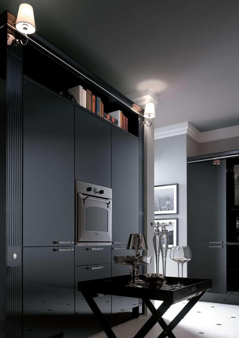 Modern kitchen interior with dark cabinets, built-in oven, decorative lighting, and a small table with glassware.