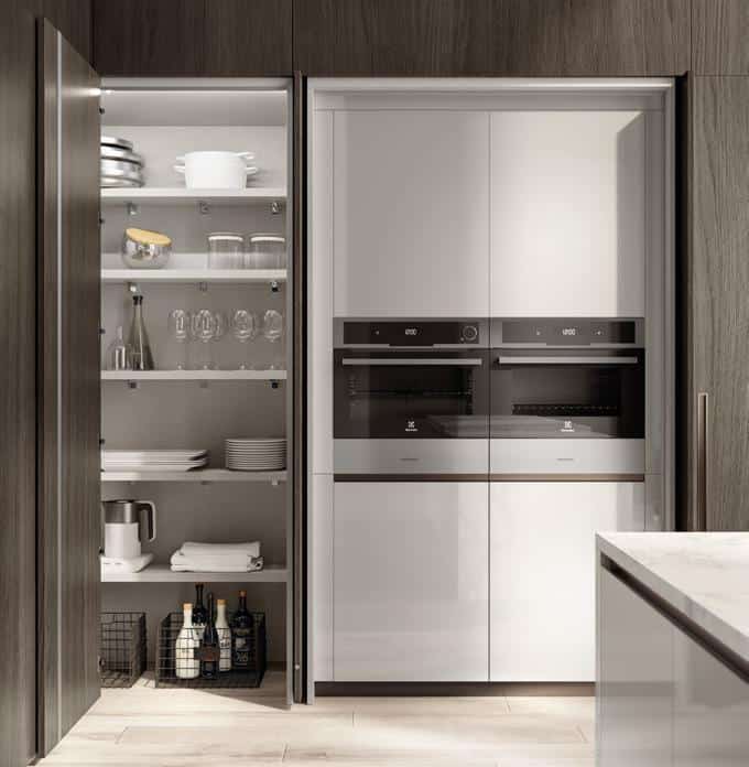 Modern kitchen with built-in ovens, open pantry with shelves of glassware and crockery, and wooden cabinetry.
