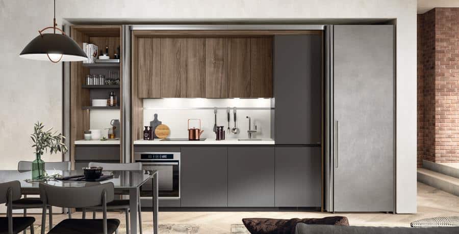 Modern kitchen with dark cabinets, wooden shelves, built-in oven, and dining table with chairs, featuring sleek, minimalist design.