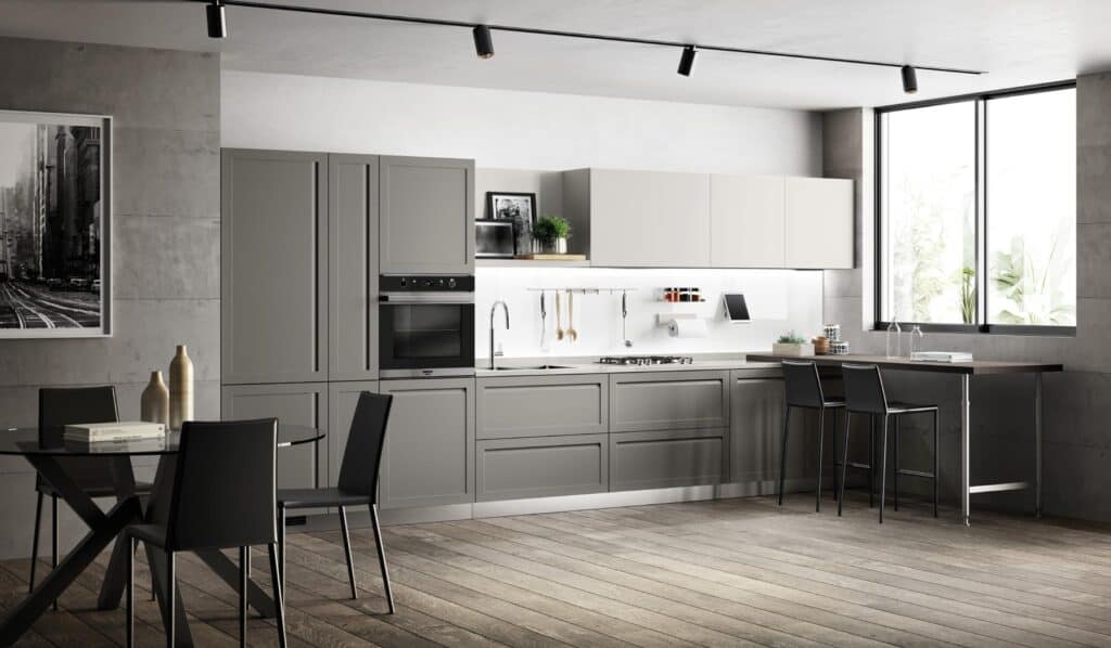 Modern kitchen with sleek gray cabinetry, a built-in oven, and a minimalistic design. A dining table with black chairs is in the foreground, and a large window provides natural light.