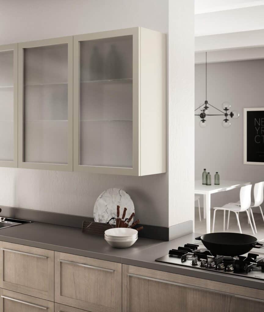 Modern kitchen with wooden cabinets, glass-fronted cupboards, a black stovetop, white bowls, and a dining area in the background.