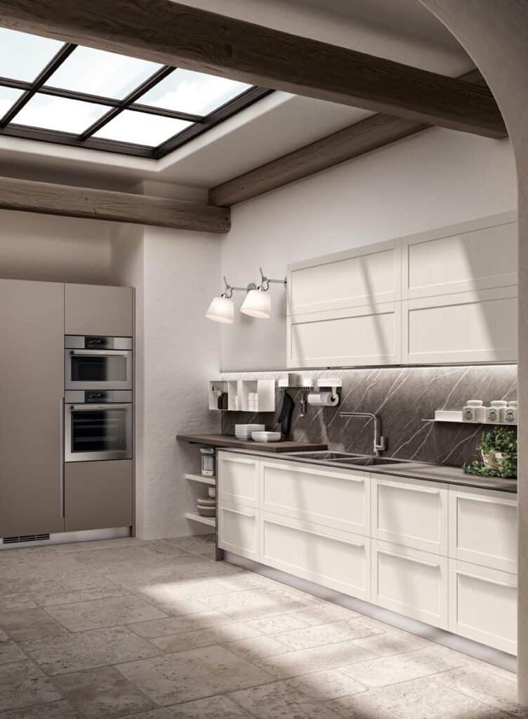 Modern kitchen with white cabinetry, dark countertops, built-in ovens, and a skylight, featuring a tiled floor and wall-mounted shelves.