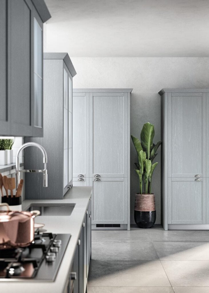 Modern kitchen with light gray cabinets, a stainless steel sink and faucet, a stovetop with a copper pot, and a large potted plant.