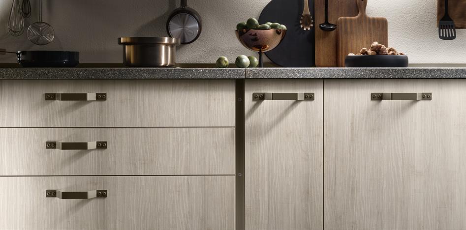 Modern kitchen cabinets with metal handles below a countertop with cookware, utensils, and decorative items.