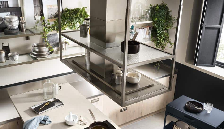 Modern kitchen interior with floating shelves, stainless steel appliances, potted plants, a countertop with kitchenware, and natural light from a window.