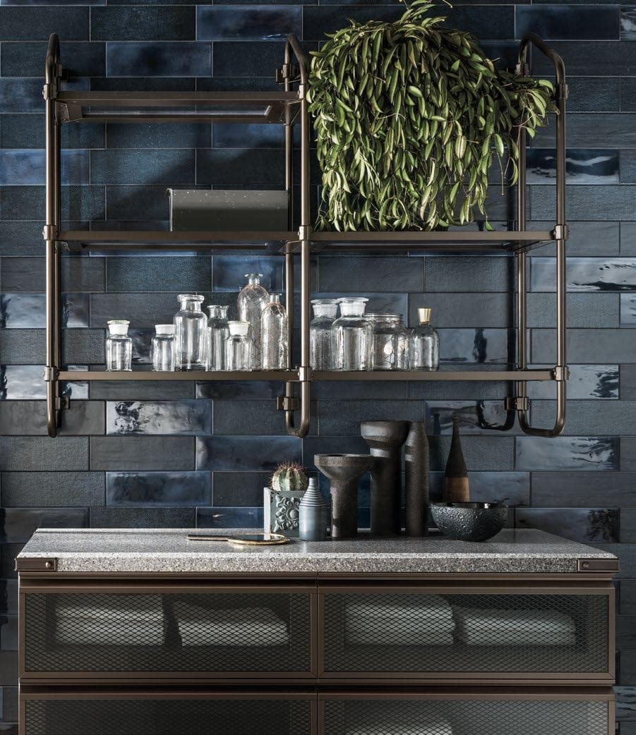 A kitchen with a dark tiled backsplash, metal shelves holding glass jars and a leafy plant, and a countertop with decorative items.