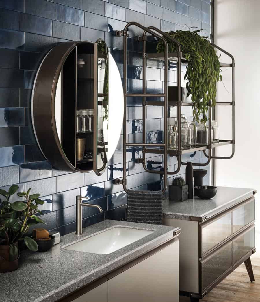 Modern bathroom with blue tiled wall, circular mirror with cabinet, glass shelf with plants, and a sleek sink on a gray countertop.