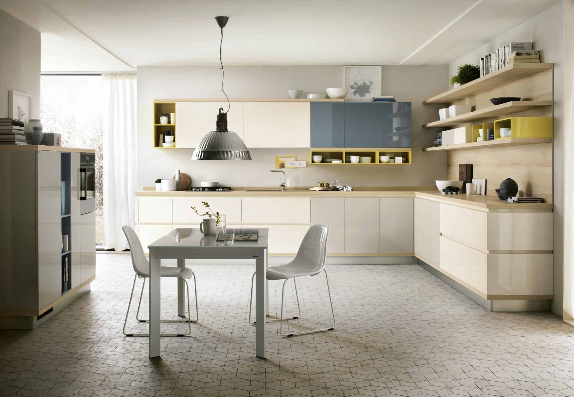 Modern kitchen with beige and blue cabinets, white dining table with two chairs, geometric patterned floor, and pendant light.