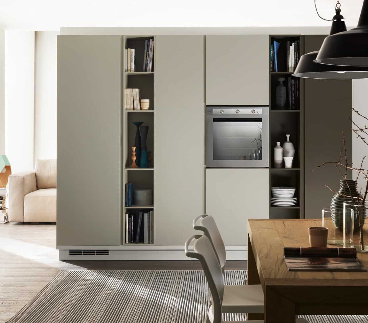 Modern kitchen with built-in oven, open shelves with books and decor, wooden dining table, and chairs.