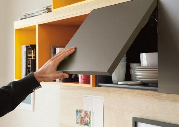 Person opening a modern kitchen cabinet with white dishes inside.
