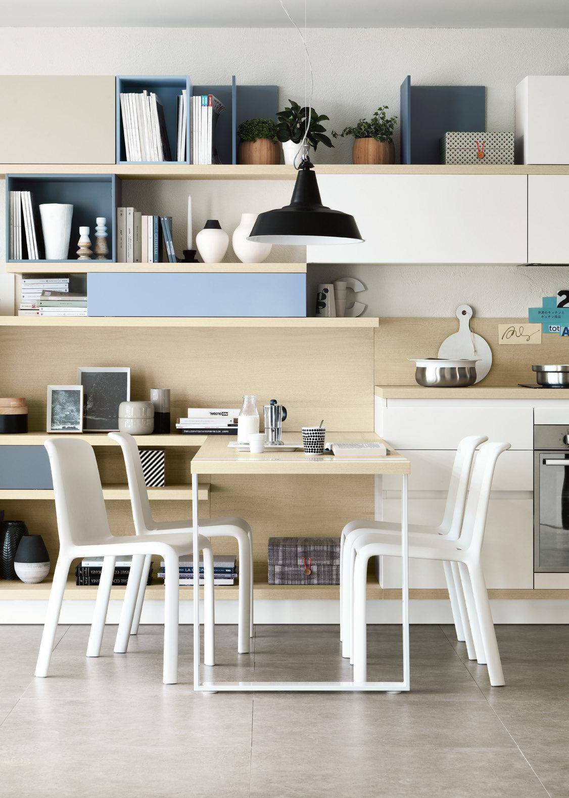 Modern dining area with white chairs, a wooden table, open shelving with books and decor, and a black pendant light.