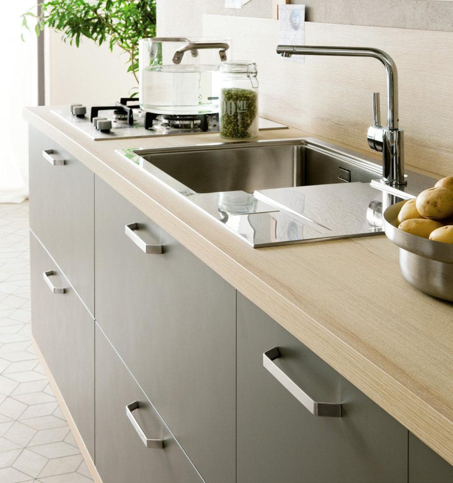 Modern kitchen with a light wood countertop, stainless steel sink, chrome faucet, gas stove, and a bowl of potatoes.