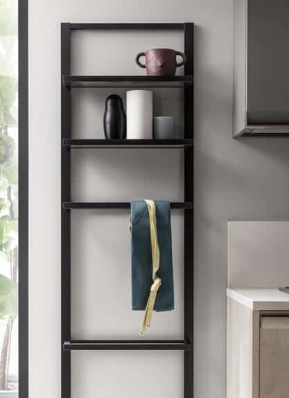 Black ladder shelf with mugs, vases, and a towel hanging, against a light gray wall.