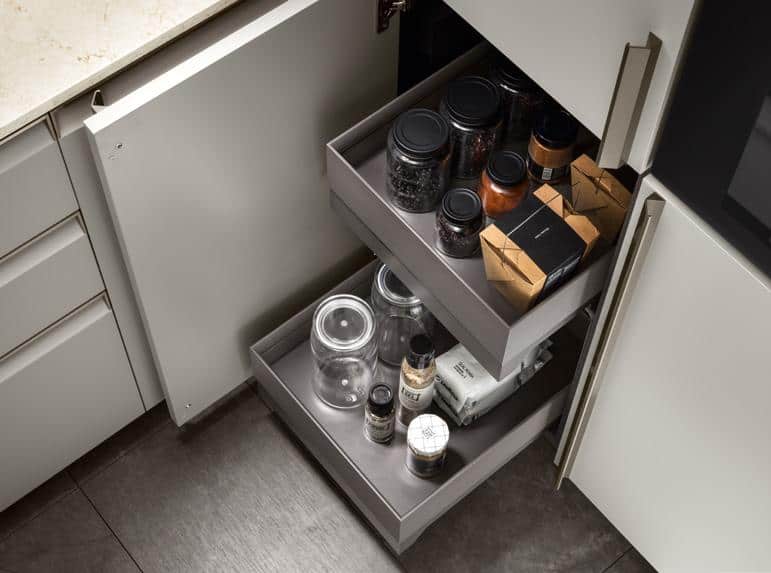 A kitchen cabinet with open sliding drawers holding jars and packages.