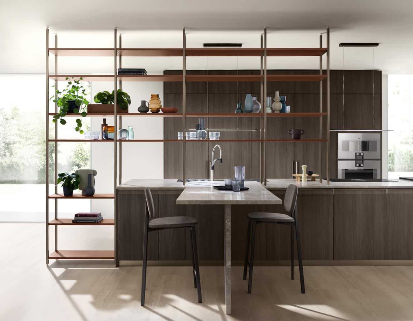 Modern kitchen with open shelving, greenery, a bar-style island with two chairs, and built-in appliances on wood cabinetry.