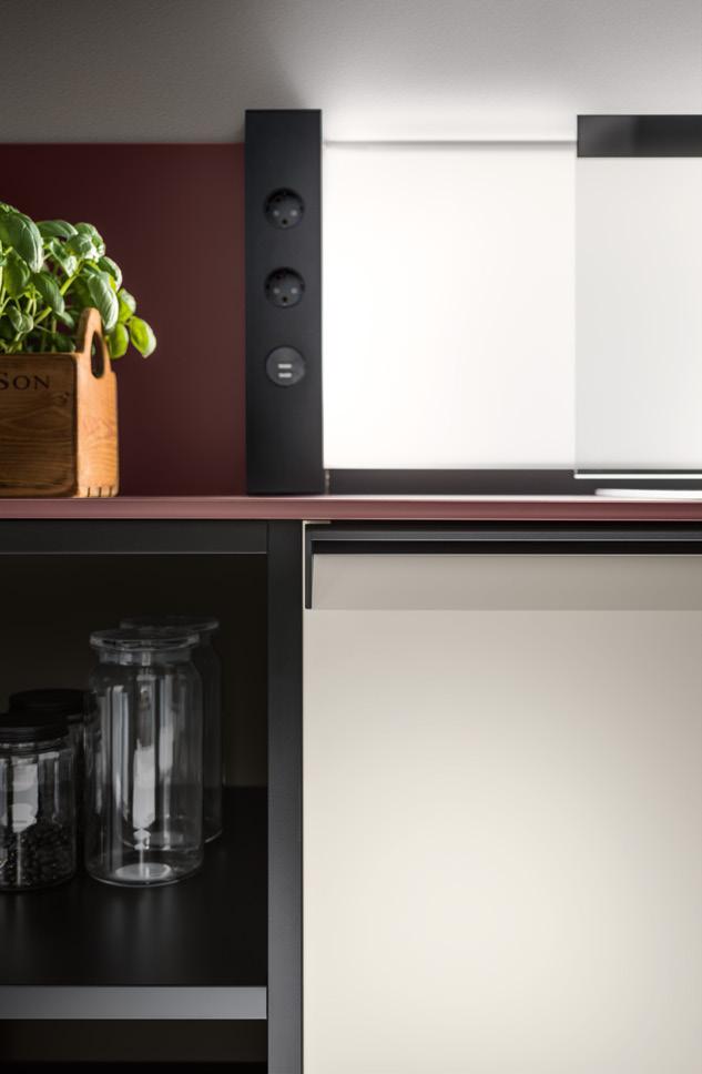 A modern kitchen counter with a potted basil plant, a power outlet panel, and glass jars on a shelf below.